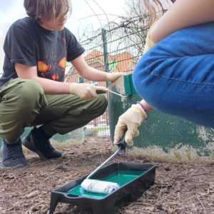 2 Kinder streichen einen Betonring mit grüner Farbe