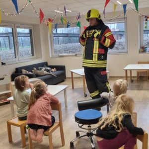 Feuerwehrmann in Uniform steht vor einer kleinen Kindergruppe