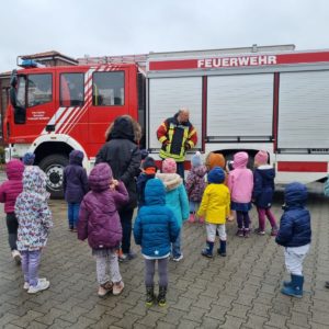 Kindergruppe und Feuerwehrmann stehen bei einem Einsatzfahrzeug